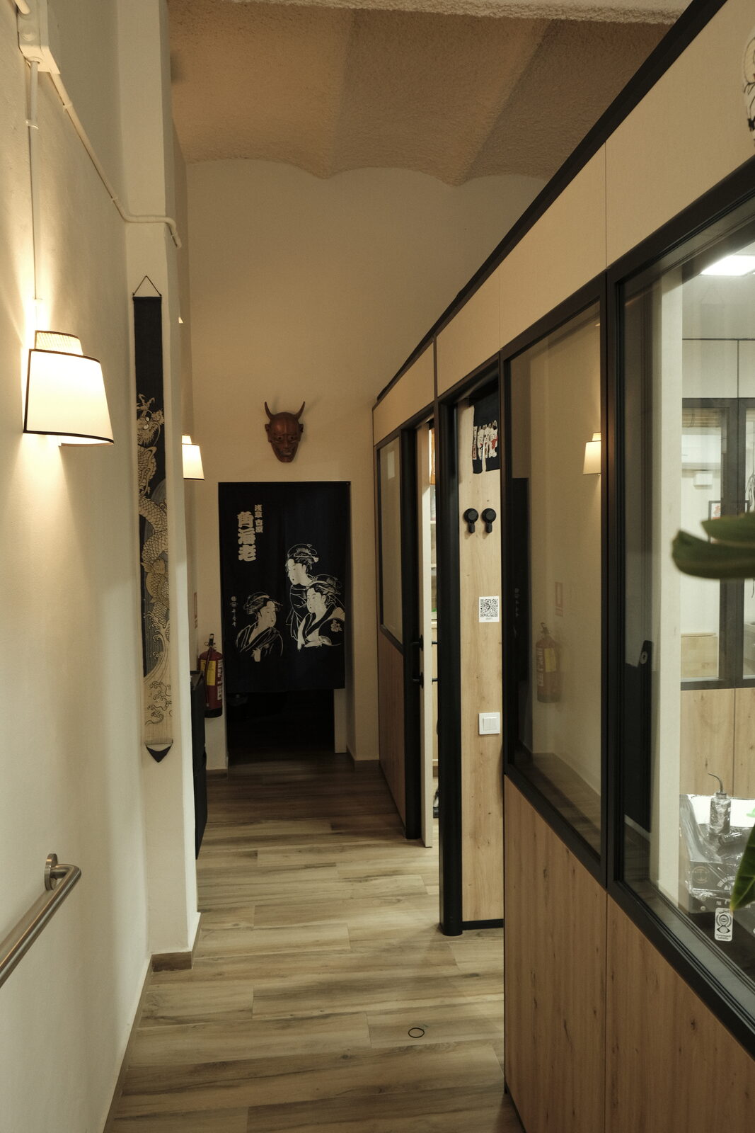 Pasillo del estudio con cabinas de tatuaje acristaladas y cortina noren japonesa