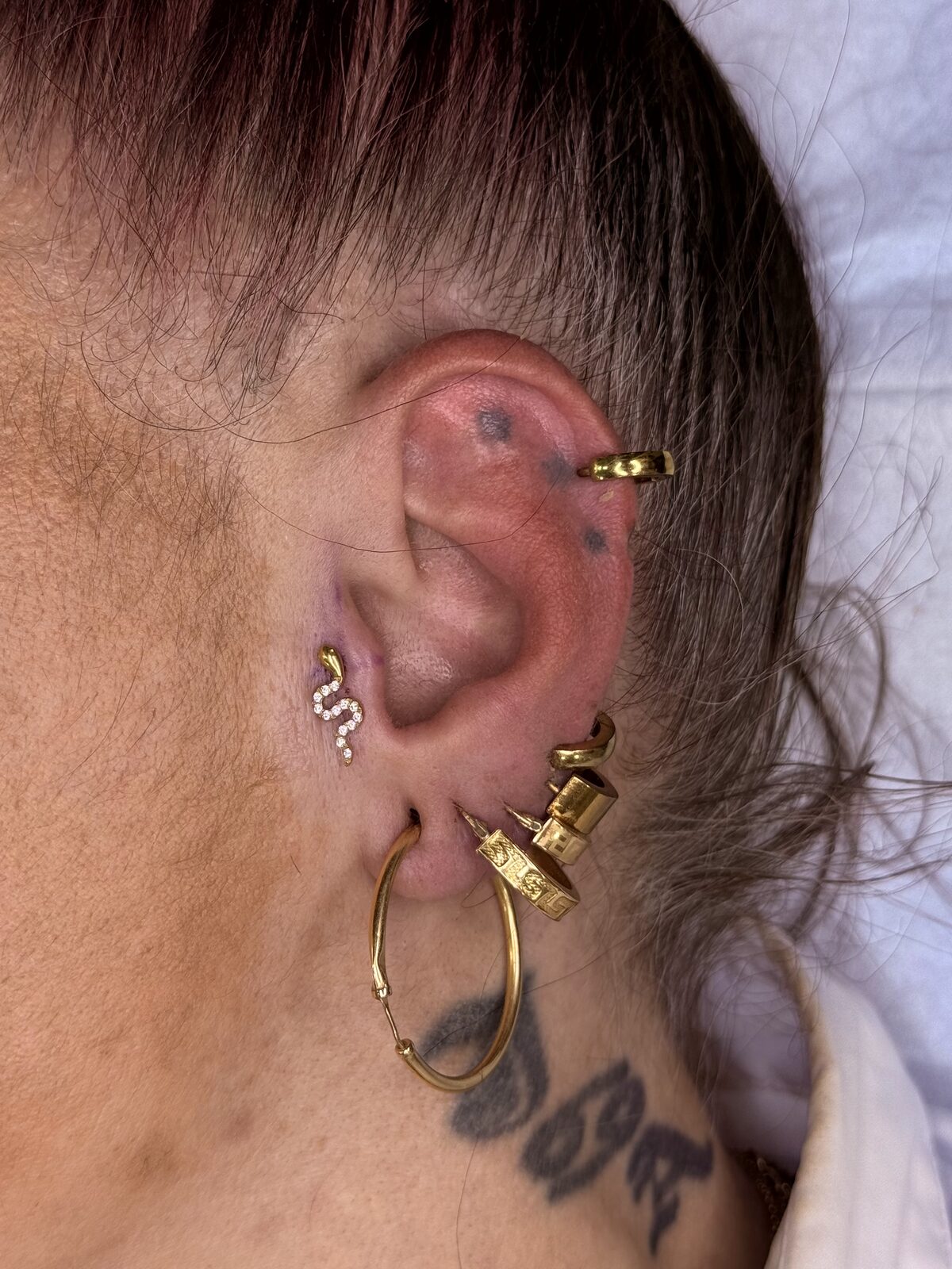 Oreja con varios piercings y joyas doradas