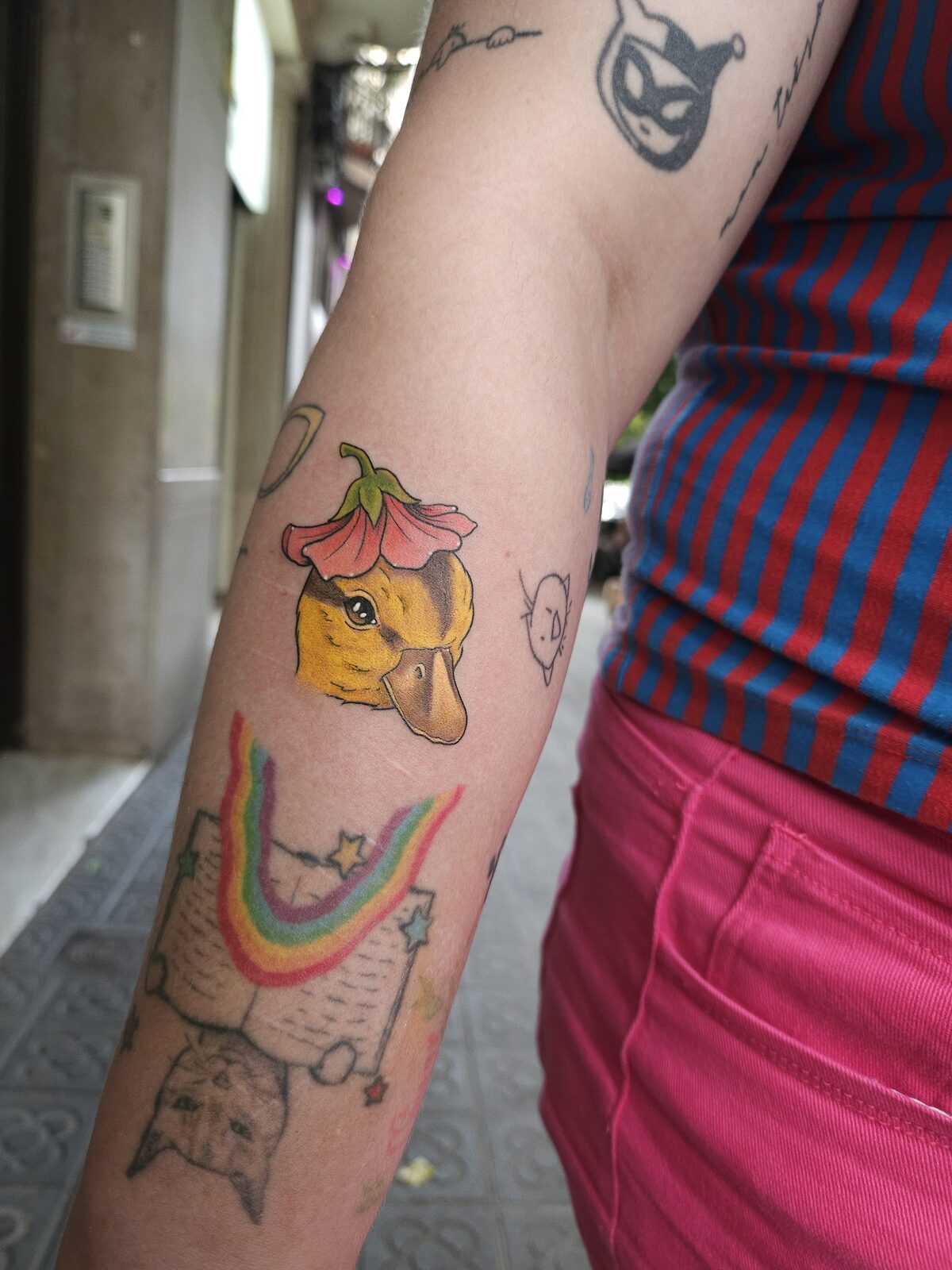 Pato amarillo con gorro de flor y otros tatuajes pequeños en el antebrazo