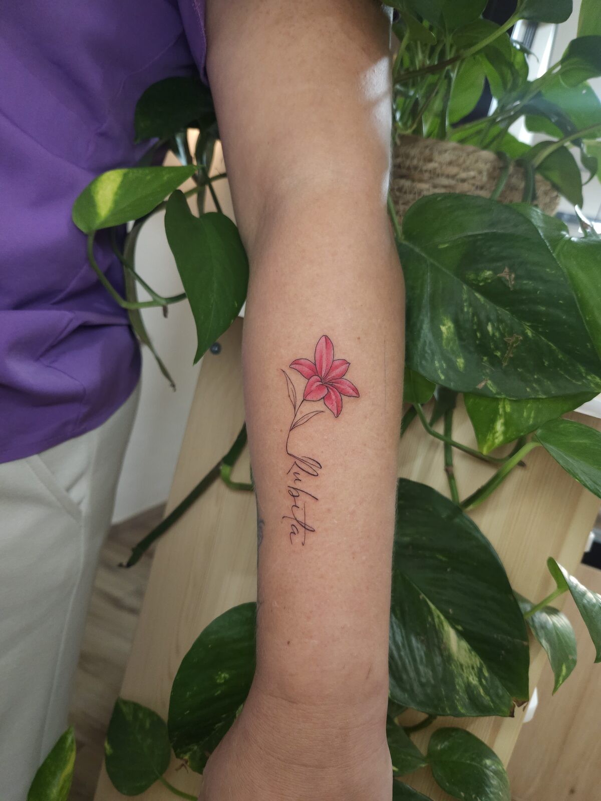 Lirio rosa con lettering en línea fina en el antebrazo