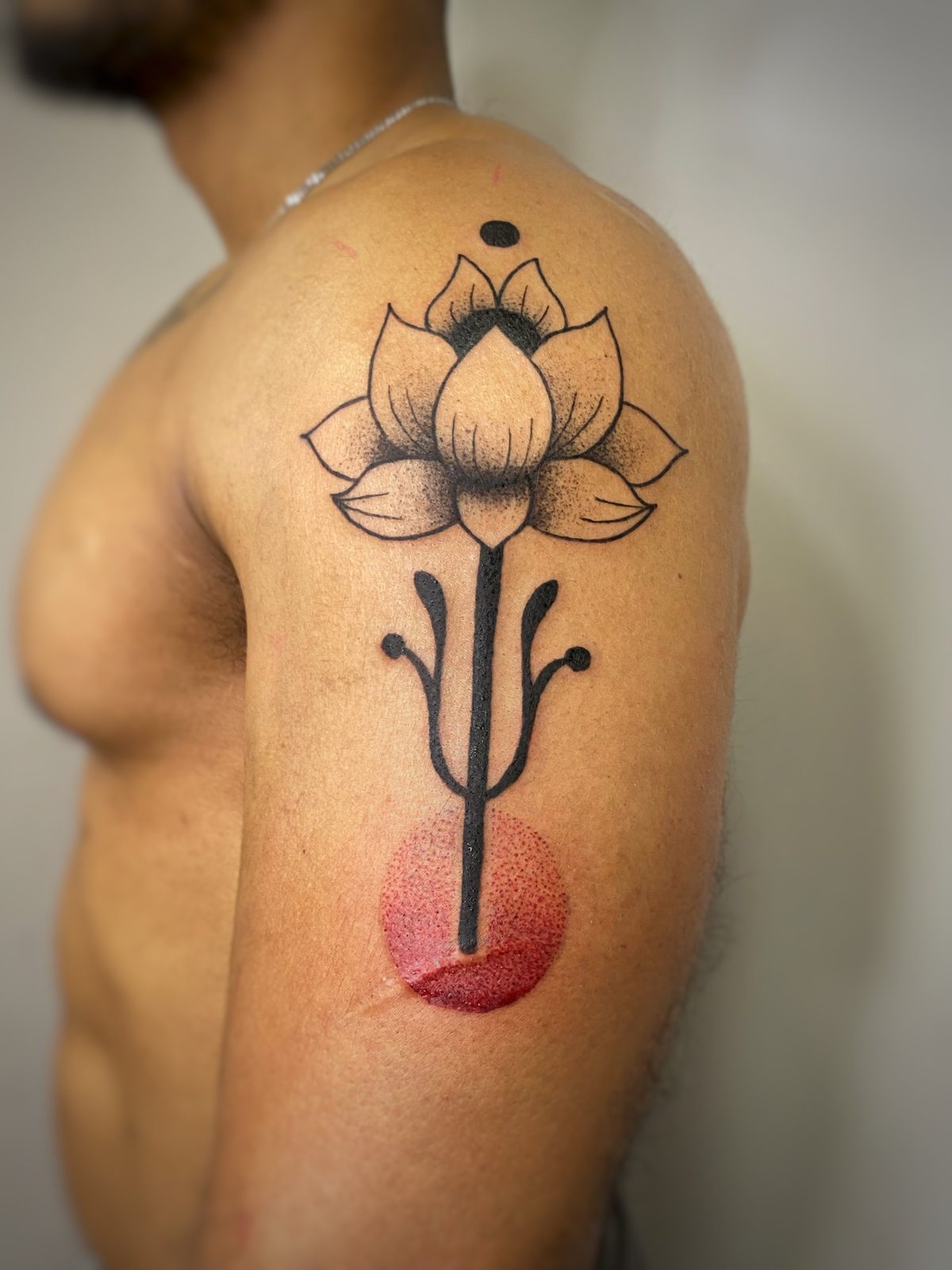 Flor de loto en negro con punteado y círculo rojo en el hombro