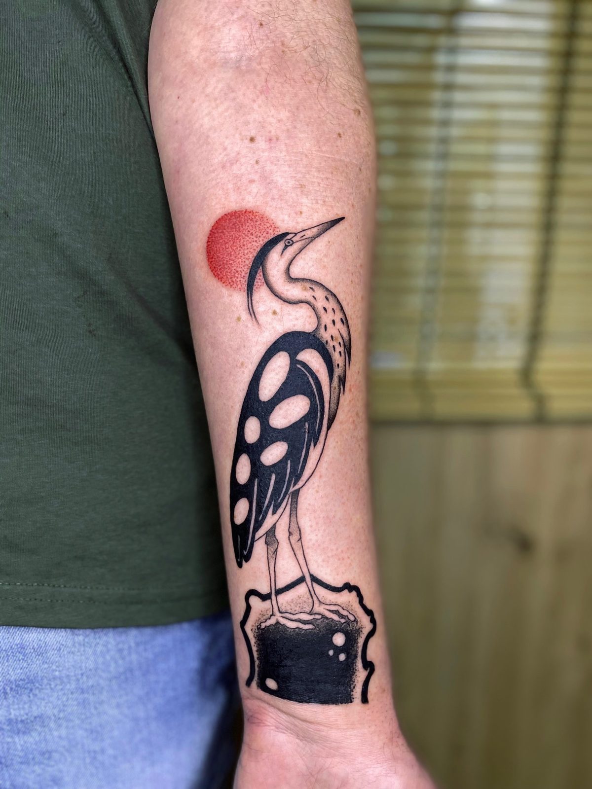 Garza en blackwork con sol rojo punteado en el antebrazo