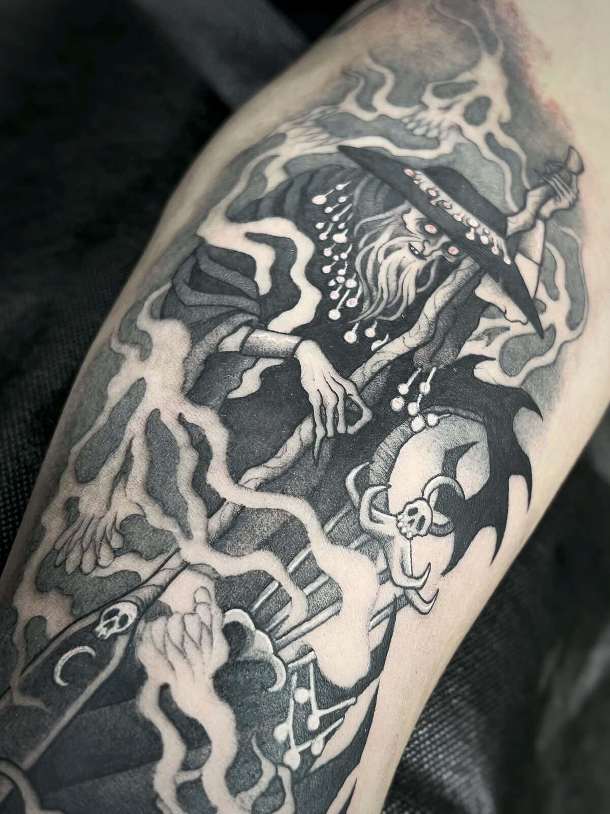 Mago con calaveras y rayos en negro y grises en el antebrazo