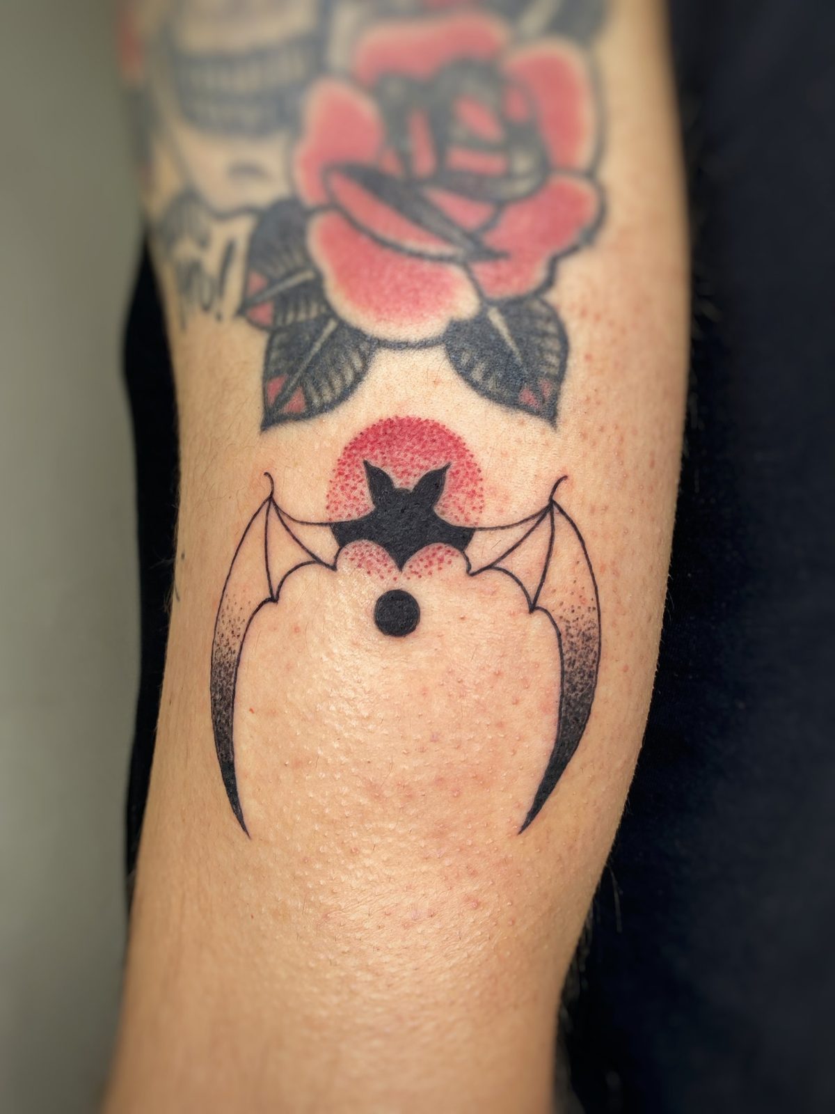 Murciélago en negro con alas abiertas y punteado rojo en el brazo