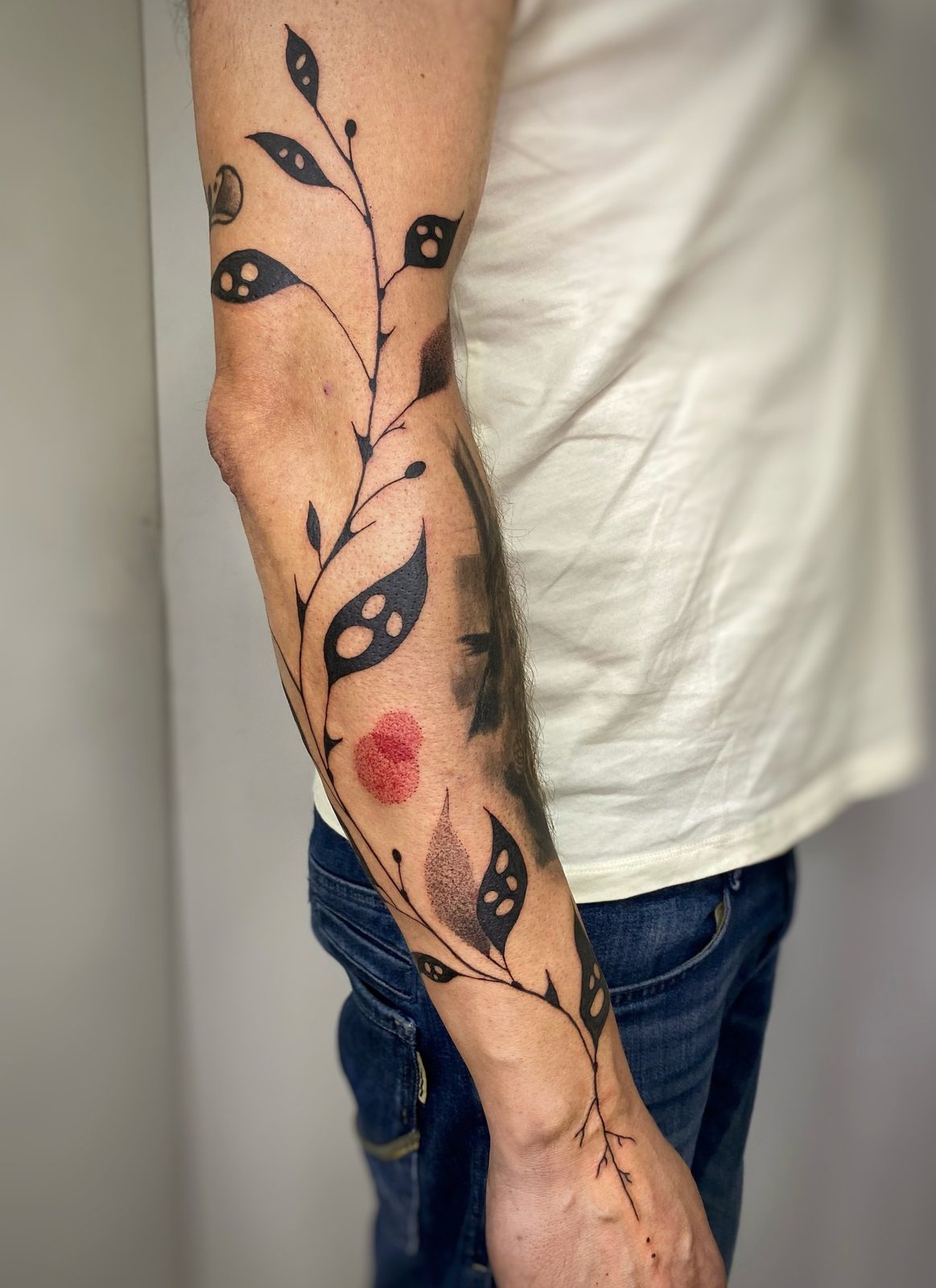 Rama de hojas negras con punto rojo a lo largo del antebrazo
