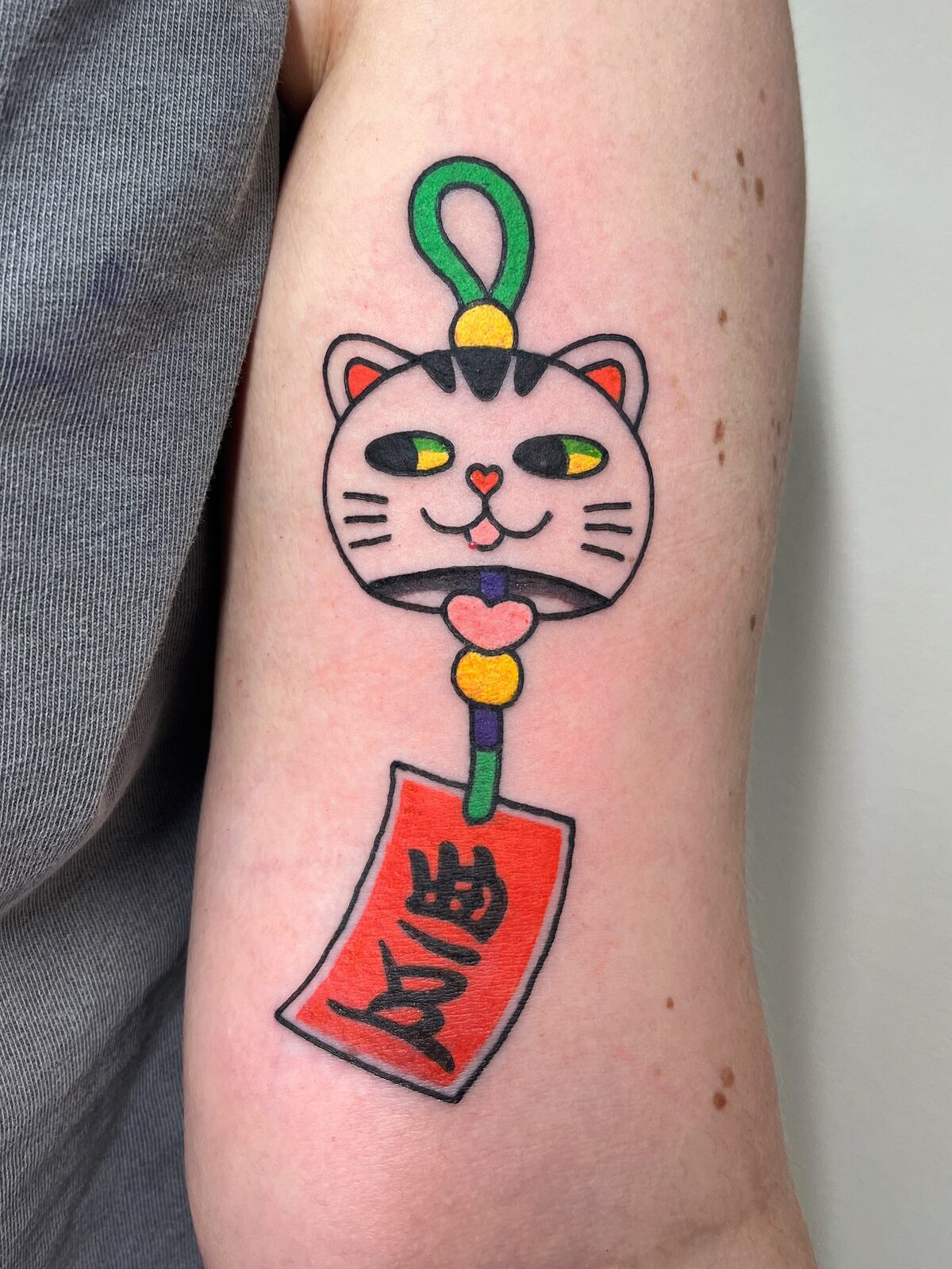 Amuleto japonés con cara de gato y tablilla roja en el brazo