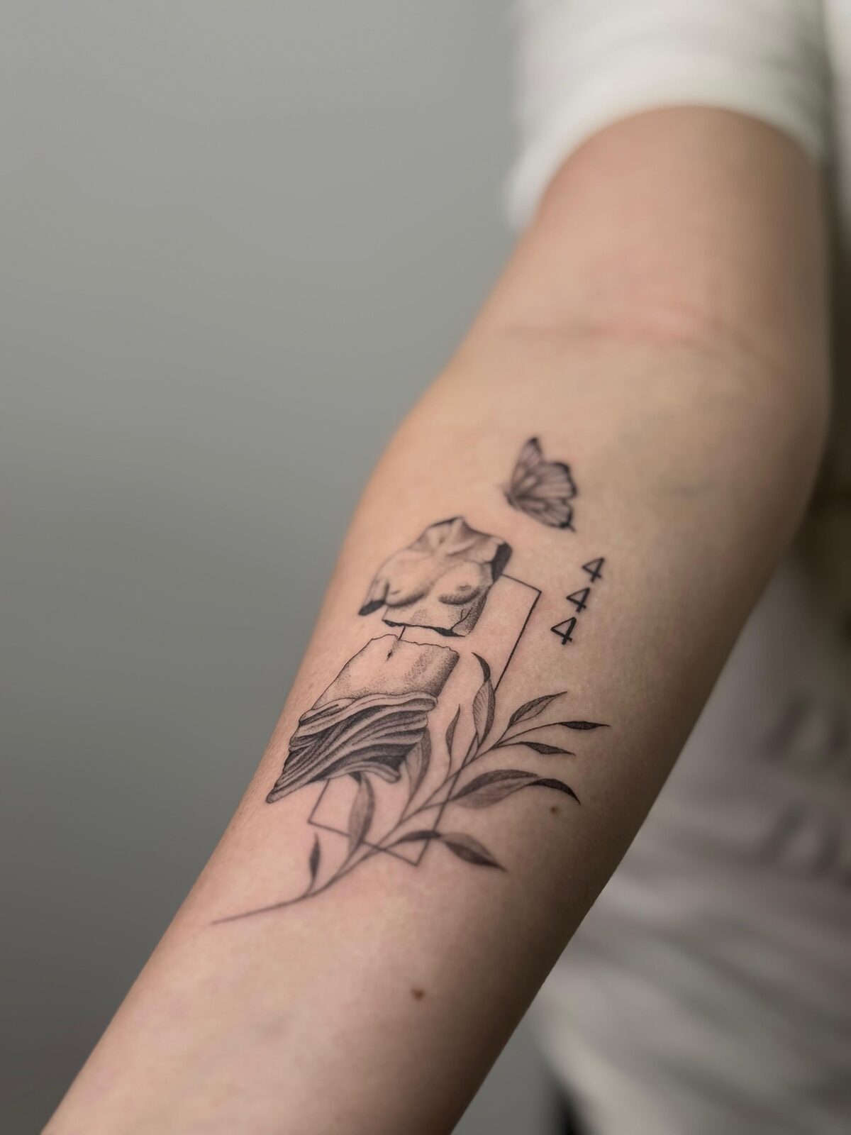 Fragmento de escultura con libro, mariposa y número 444 en el antebrazo