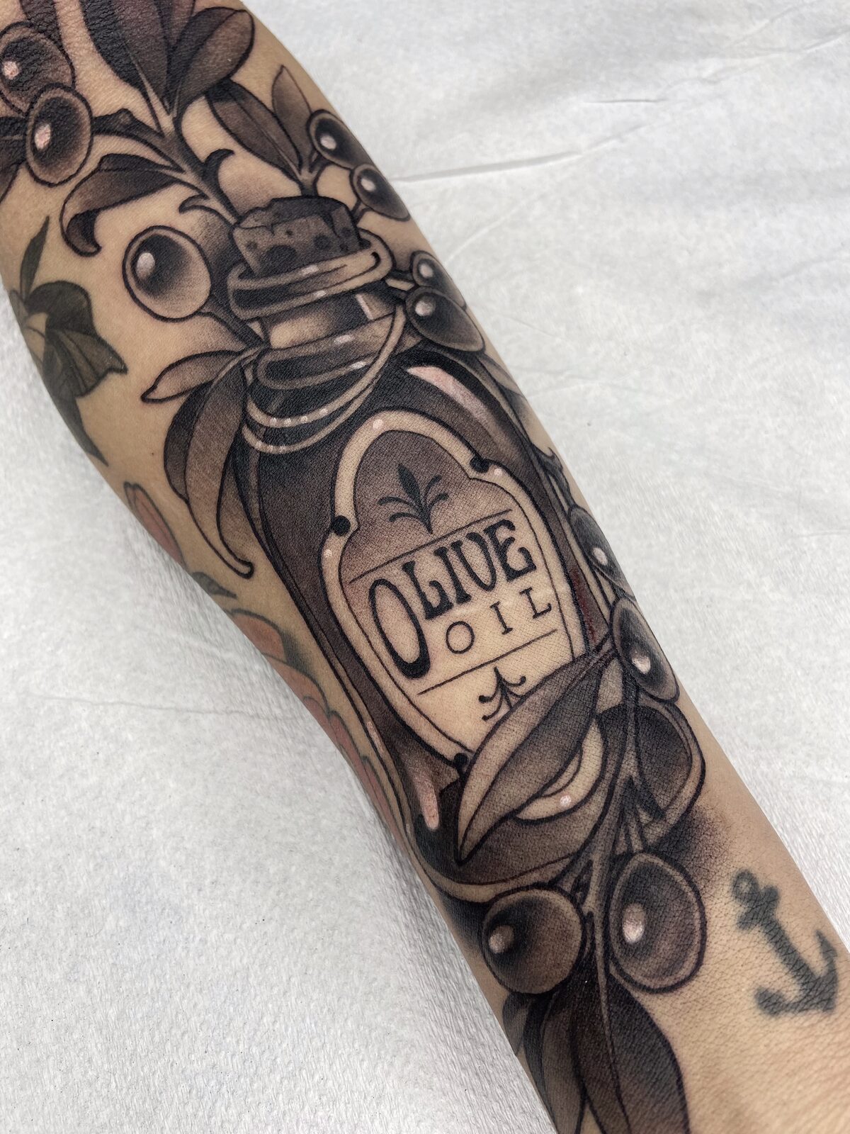 Botella de aceite de oliva con aceitunas en negro y grises en el antebrazo