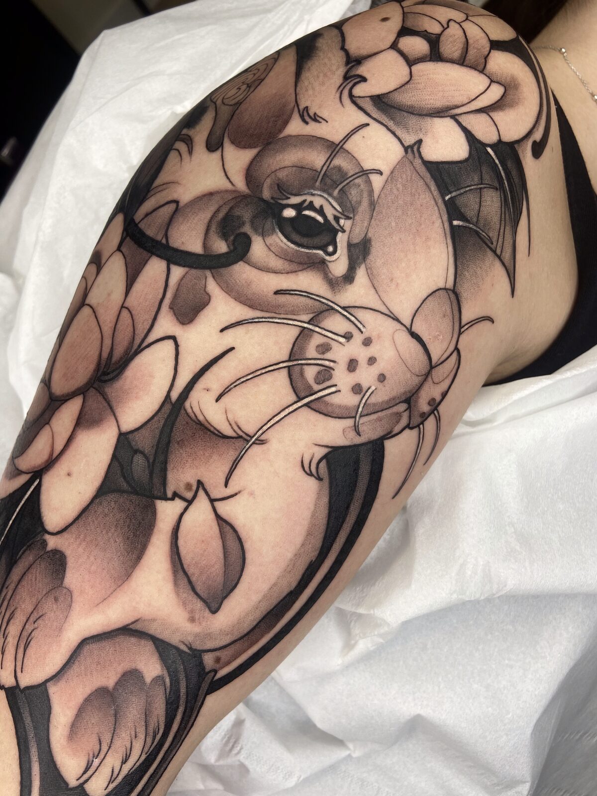 Gato con alas de murciélago y flores de loto en negro y grises en el brazo