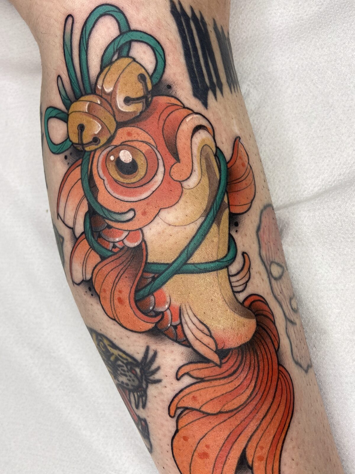 Pez dorado con cascabeles en estilo neotradicional en el antebrazo